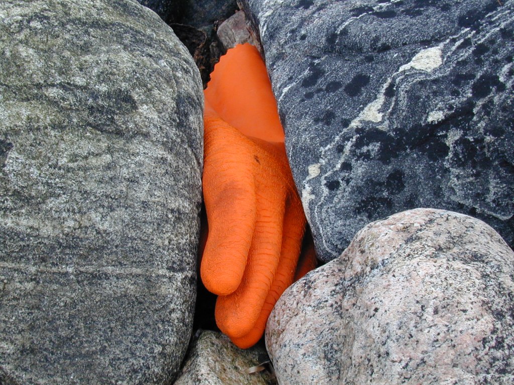 Photography of an orange glove  between round rocks.